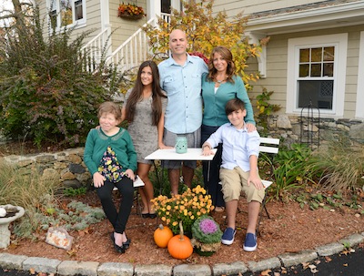 Family, including person who is participating in shared living, posing in front or their home